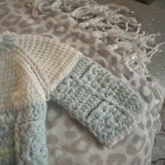 blue and white crochet baby cardigan with pom-pom ties and embroidered flowers.